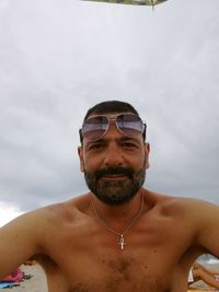Portrait of confident shirtless man wearing sunglasses while sitting at beach