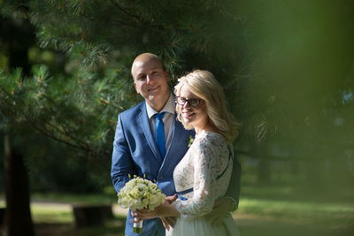 Portrait of bride and groom standing by trees at park