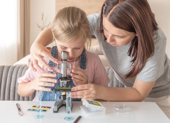 Mother helping daughter to look into microscope at home