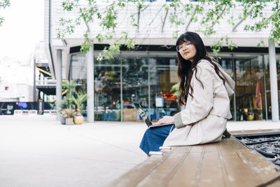 Young woman wearing eyeglasses sitting with laptop in city