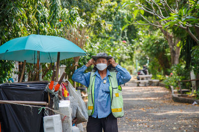 An old asian man street cleaner wearing masks before going to work next to an old garbage cart 