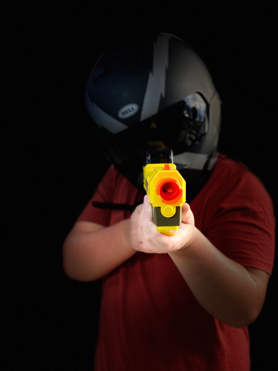 one person, holding, black background, studio shot, red, waist up, indoors, helmet, yellow, headwear, mask, toy, child, men, standing, portrait, front view, sports, childhood, adult, disguise, obscured face, clothing