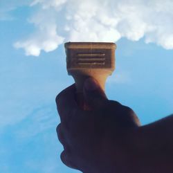 Low angle view of hand holding cross against sky