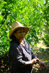 Senior woman wearing hat standing against plants in farm