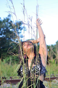 Portrait of woman with arms raised on field against sky