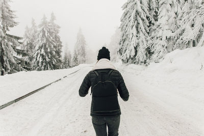 Rear view of man with backpack walking on snow covered land