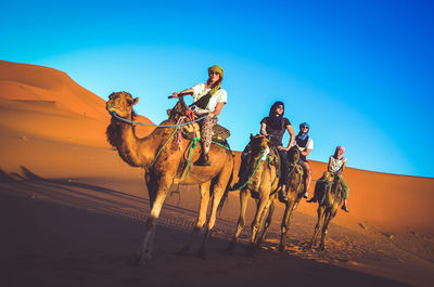 Men riding horse in desert against sky