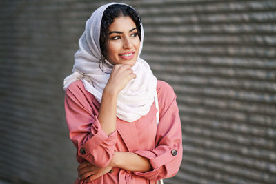 Portrait of a smiling young woman standing against wall