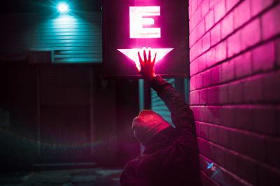 Rear view of woman touching neon sign by wall at night