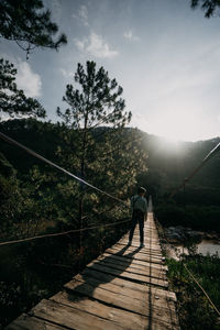 Man walking on footbridge against sky