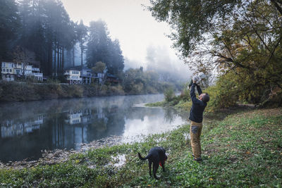 A man is holding a baby near a river and a dog