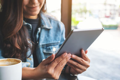 Midsection of woman using digital tablet while having coffee in cafe