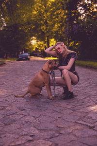 Young woman crouching by dog on footpath