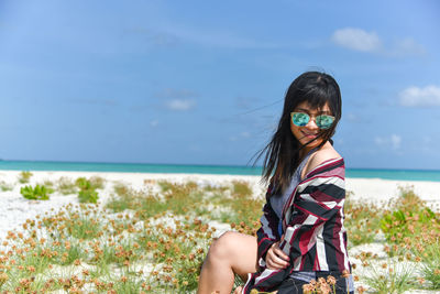 Portrait of smiling young woman standing by sea against sky