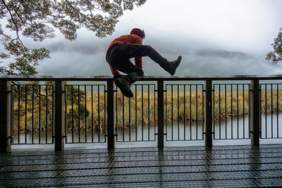 Full length of man jumping over fence against cloudy sky
