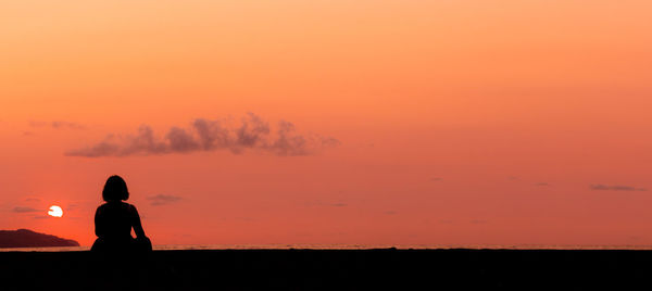 Woman sitting at beach, watching the sunset, silhouette.