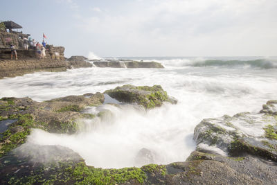 Scenic view of sea waves splashing on rocks against sky