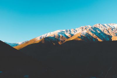 Low angle view of snowcapped mountains against clear blue sky