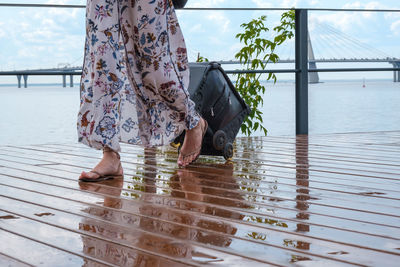 Low section of woman with umbrella on railing against sky