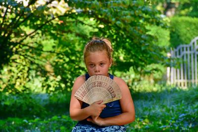 Portrait of girl holding folding fan against trees