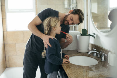Mid adult father brushing daughter's teeth at sink in bathroom