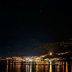 Illuminated city by sea against sky at night