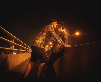 Side view of boyfriend kissing on girlfriend forehead in city at night