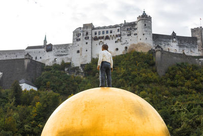 Rear view of man standing by building against sky