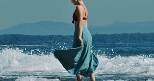 Full length of shirtless woman standing in sea against sky