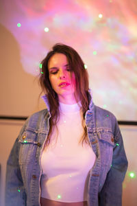 Portrait of beautiful woman standing against illuminated wall