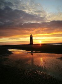 Silhouette lighthouse on shore at beach against sky