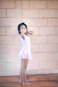 Portrait of girl holding slingshot standing against wall