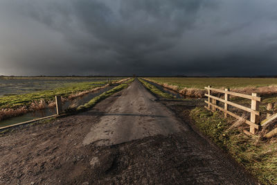 Dirt road amidst field against sky