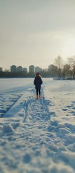 Rear view of a girl in red santa's hat walking on snow covered landscape.