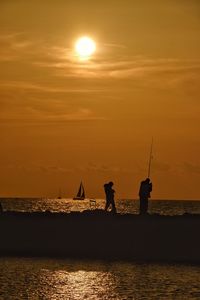 Silhouette man fishing in sea against orange sky