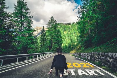 Rear view of man walking on road against trees