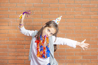 Portrait of girl wearing party equipment against brick wall