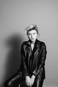 Portrait of young woman sitting against gray background