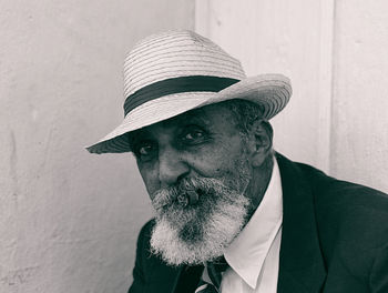 Portrait of man smoking cigar while sitting against wall