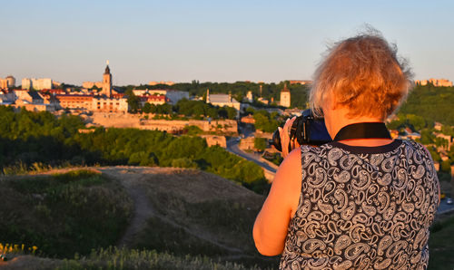 Rear view of female photographer photographing buildings against clear sky during sunset