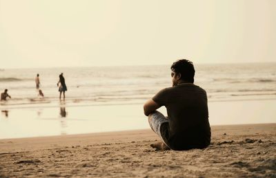 Man sitting on beach against clear sky