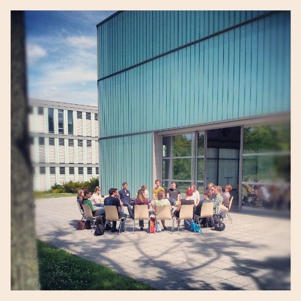 transfer print, building exterior, architecture, built structure, auto post production filter, men, person, city, lifestyles, leisure activity, sky, large group of people, city life, grass, sitting, day, sunlight, building, chair