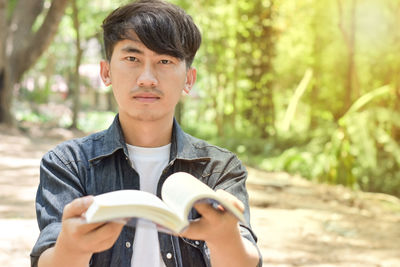 Portrait of young man holding sunglasses against trees