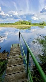 Wooden railing by lake against sky