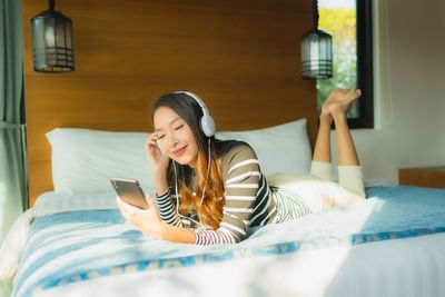 Young woman using mobile phone on bed at home