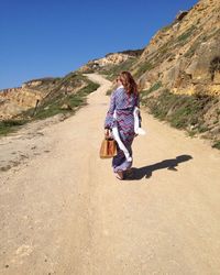 Full length rear view of woman walking on dirt road