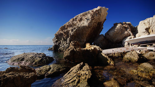 Rock formations at sea shore against blue sky