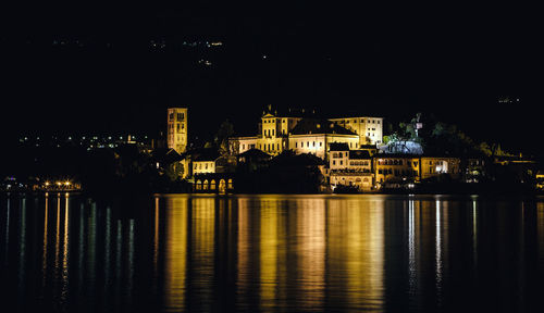 Illuminated city by river against sky at night