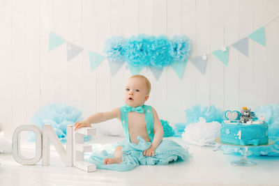 A one-year-old boy in blue shorts and a bow tie celebrates his birthday next to the letters one 