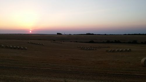 Hay bales on field against sky during sunset